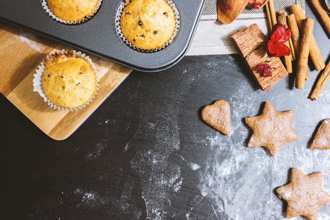 A delicious arrangement of muffins and cookies with cinnamon and flour on a black countertop.