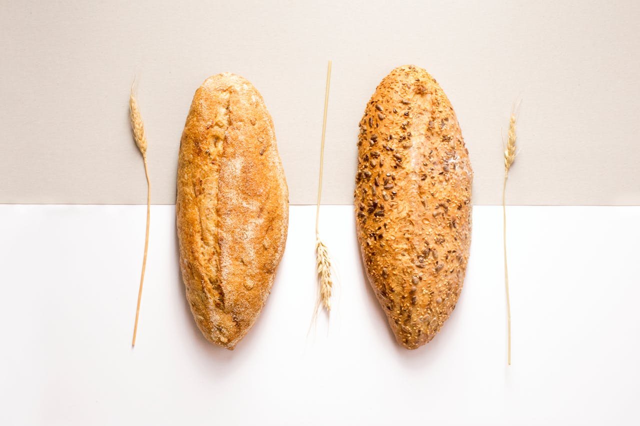 Flat lay image of two artisan bread loaves with wheat decoration on a neutral background.